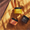 Drei Tiegel Pore Cleansing Balm von Hanskin liegen auf gelbem Stoff und werden vom Sonnenlicht beleuchtet.