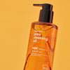 Eine orangefarbene Flasche Pore Cleansing Oil AHA mit einer schwarzen Pumpe vor einem orangenen Hintergrund.