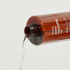 Braune Flasche Pore Cleansing Oil BHA mit herausfließender Flüssigkeit vor einem schlichten Hintergrund.