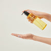 Eine Hand gibt vor einem schlichten Hintergrund Flüssigkeit aus der Flasche Pore Cleansing Oil PHA auf ihre Handfläche.