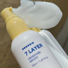 Eine Flasche Seven Layer Ceramide Serum liegt auf der Seite, dahinter ist weißes Serum verteilt.