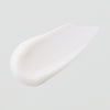 Ein glatter Fleck der weißen Textur der Vitamin A Glow Retinol Cream auf hellgrauem Hintergrund.