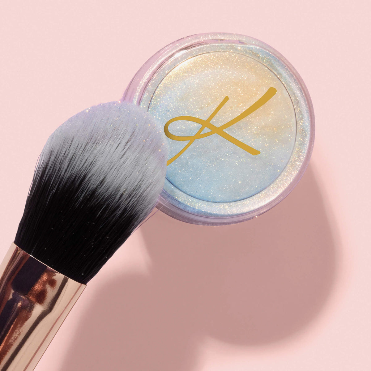 Der K10: Highlighter Brush neben einem transparenten Glitter Pot Behälter auf rosa Hintergrund.