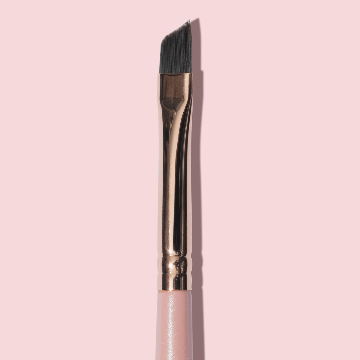 Nahaufnahme des K26: Eyeliner Brush mit abgewinkeltes Design, rosa Griff und goldener Zwinge, abgebildet vor einem blassrosa Hintergrund.