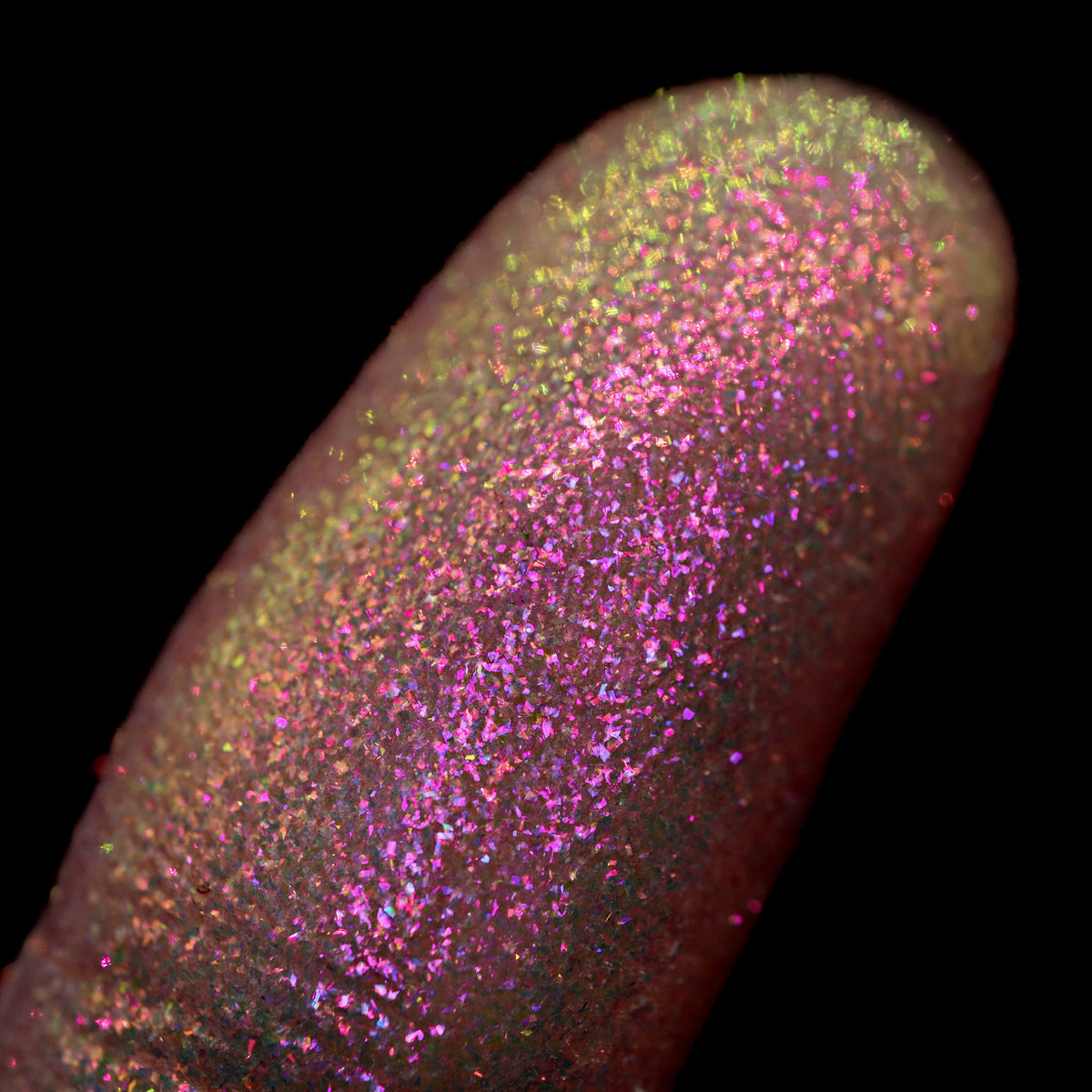 Nahaufnahme einer Fingerspitze, die in den Opal Multichrome Loose Eyeshadow Cozy getaucht wurde und gelb-grün und pink-lila glitzert.