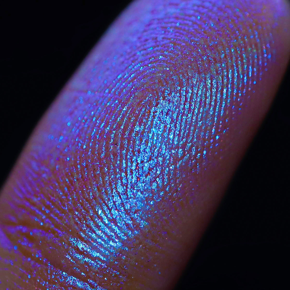 Eine Fingerspitze zeigt das Fingerabdruckmuster, das durch den blau schillernden Schimmer des Opal Shadow Potion Silky Gel Eyeshadow noch verstärkt wird.