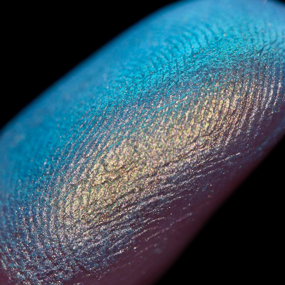 Nahaufnahme einer Fingerspitze, die in den Pastel Duochromes Loose Eyeshadow Buttons getaucht wurde und türkis und blau glitzert.
