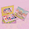 Die „Adventure Time Candy Kingdom“-Palette von Lethal Cosmetics mit leuchtenden Farbtönen und einem Spiegel sowie ihrer illustrierten Verpackung vor einem rosa Hintergrund.