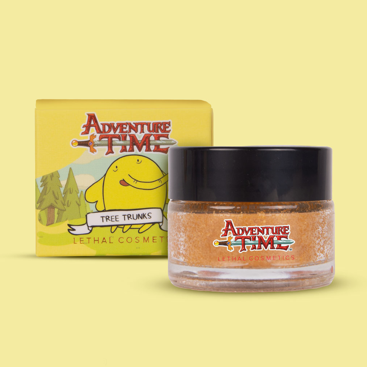 Gelbe Verpackung der Adventure Time Tree Trunks Lip Scrub mit Abbildung von Tree Trunks neben Glastiegel mit schwarzem Deckel.