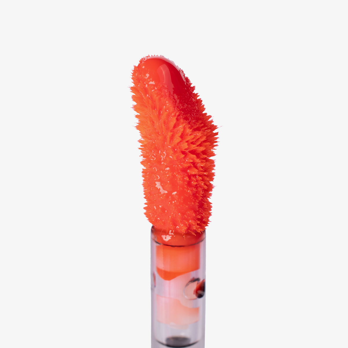 Nahaufnahme eines orangenen Lip-Stain-Applikators mit flauschiger Textur und glänzendem Produkt, freigestellt vor weißem Hintergrund.