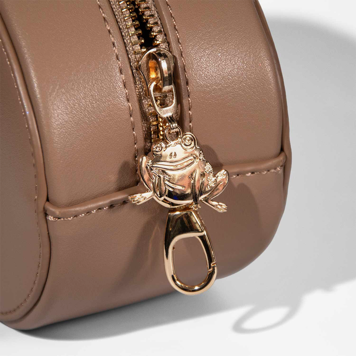 Ein goldener Frosch als Reißverschlussanhänger ziert die „Over The Garden Wall – Rock MakeUp Bag“ von Lethal Cosmetics aus sattem braunem Leder, hier in Nahaufnahme.