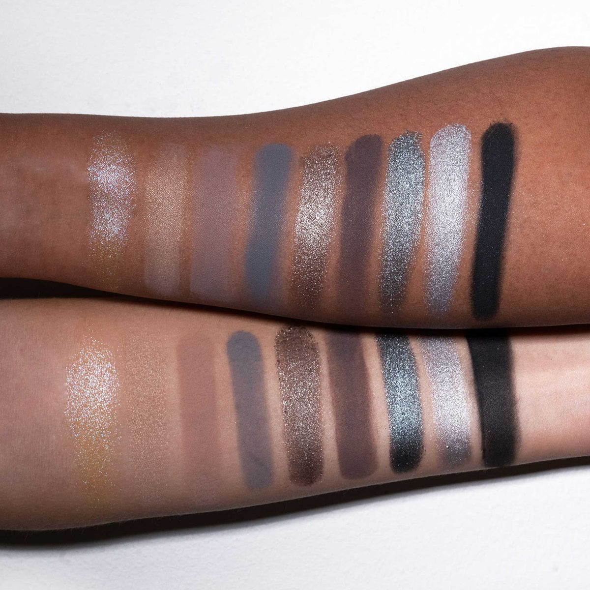 Zwei Arme mit unterschiedlichen Hauttönen präsentieren schimmernde und matte Farbtöne aus der Aim Higher Palette von LH Cosmetics.
