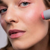 Eine Person verwendet den LH Cosmetics Artistick Blush Spalsh, um rosa Rouge auf die Wangen aufzutragen.