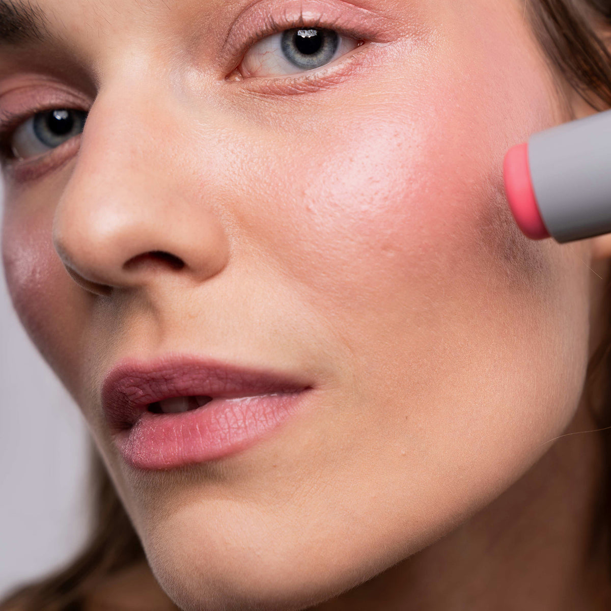 Eine Person verwendet den LH Cosmetics Artistick Blush Spalsh, um rosa Rouge auf die Wangen aufzutragen.
