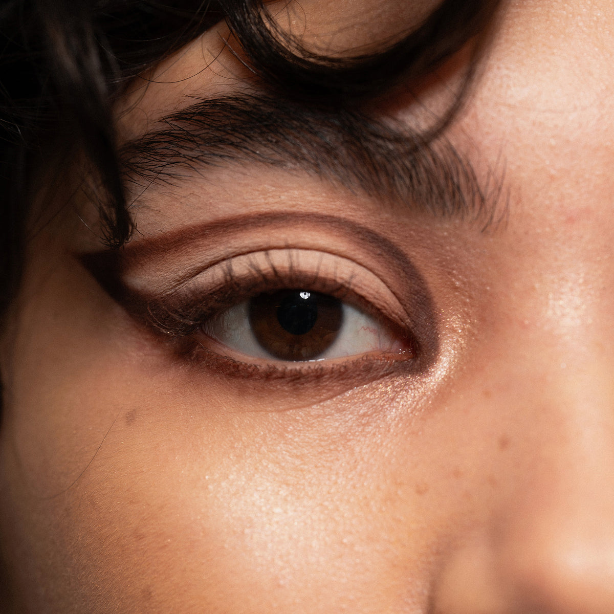 Eine Nahaufnahme eines braunen Auges mit kräftigem, grafischem Eyeliner, der mit der Boring Nude Palette von LH Cosmetics kreiert wurde.