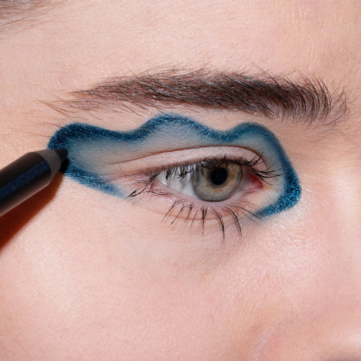 Nahaufnahme eines Auges mit wellenförmigem blau glitzerndem LH Cosmetics Crayon Atria Eyeliner-Look.