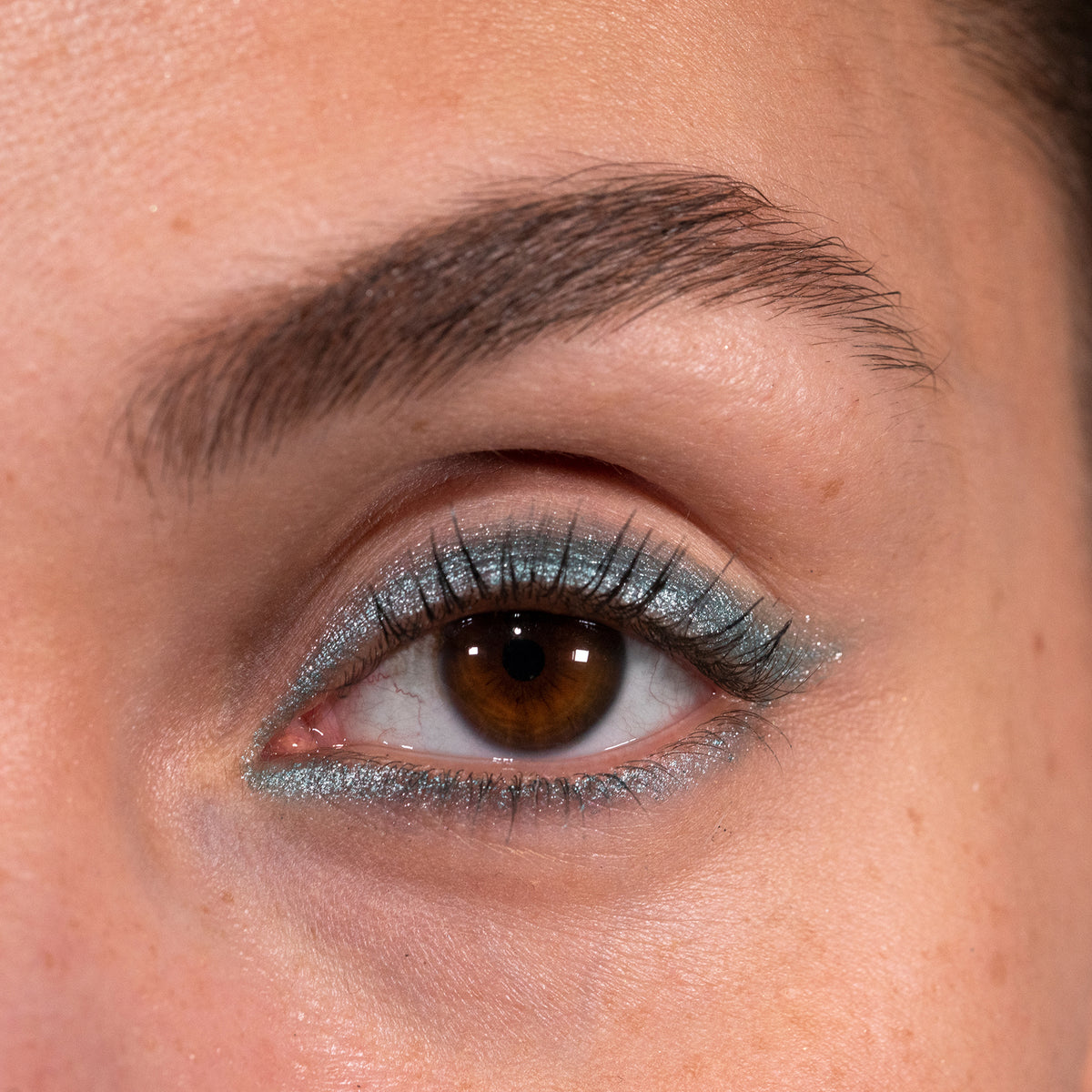 Nahaufnahme eines Auges zeigt einen kreativen türkis glitzernden Eyeliner, der mit dem Crayon Risha von LH Cosmetics kreiert wurde.