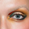 Nahaufnahme eines blauen Auges mit kräftigem grünen, goldenen und orangefarbenen Lidschatten aus der LH Cosmetics Creator Palette.