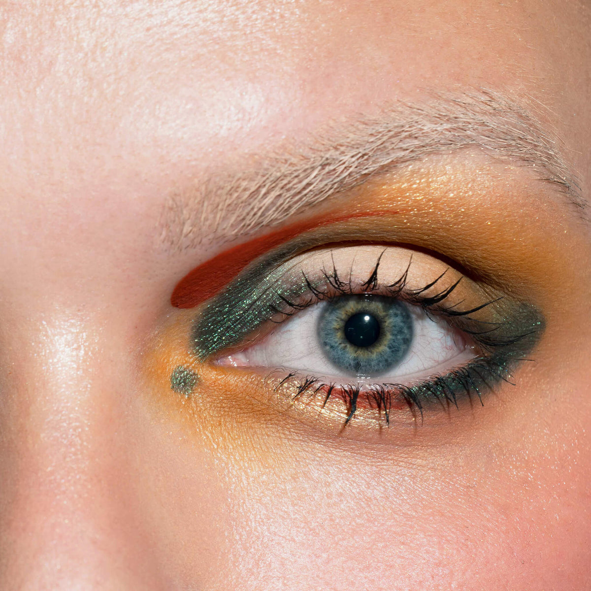 Nahaufnahme eines blauen Auges mit kräftigem grünen, goldenen und orangefarbenen Lidschatten aus der LH Cosmetics Creator Palette.