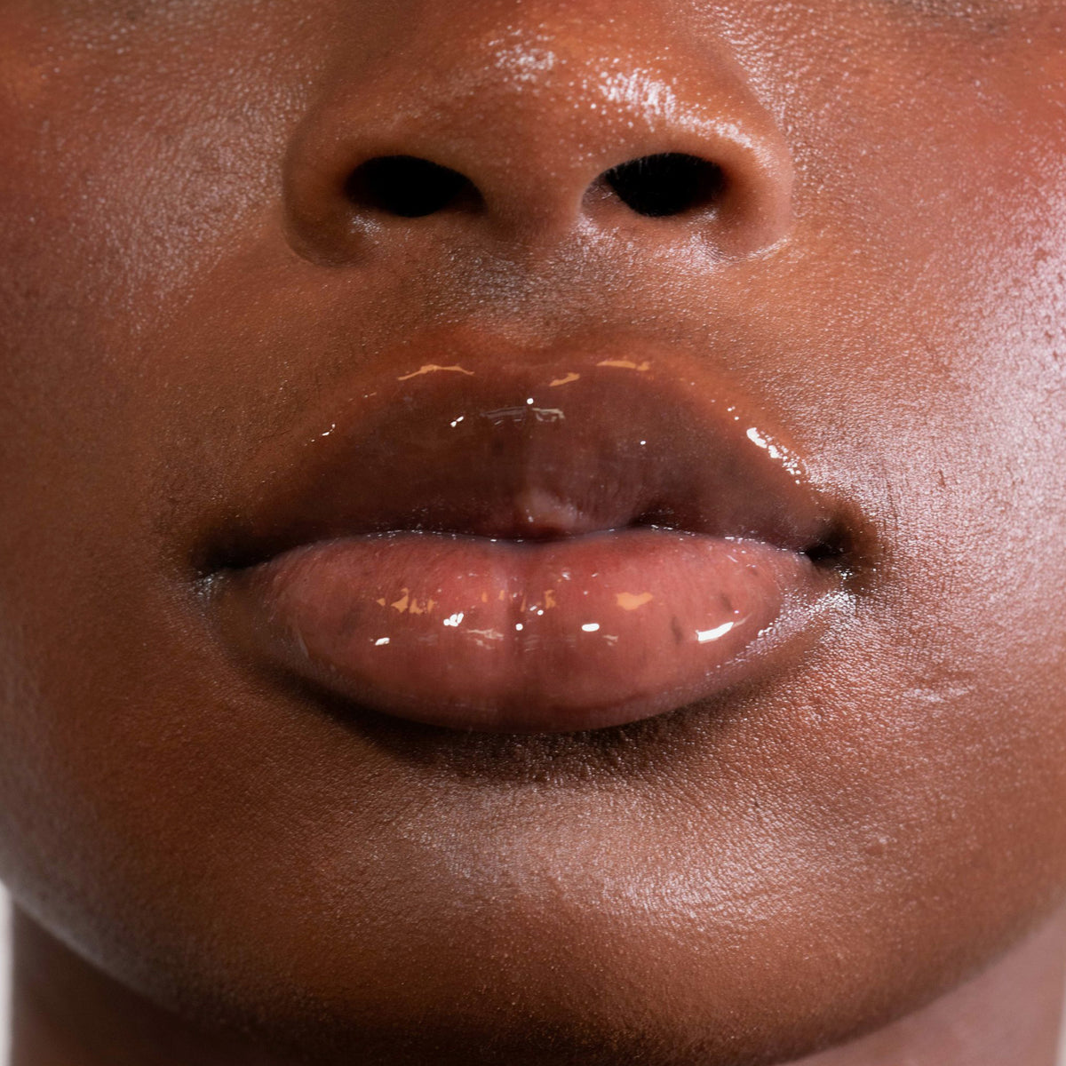 Nahaufnahme von Lippen einer Person mit dunklem Teint mit transparentem Glazed Sweet Lipgloss von LH Cosmetics.