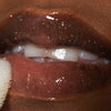Nahaufnahme von Lippen einer Person mit dunklem Teint mit transparent glitzerndem Glazed Yum Lipgloss von LH Cosmetics.