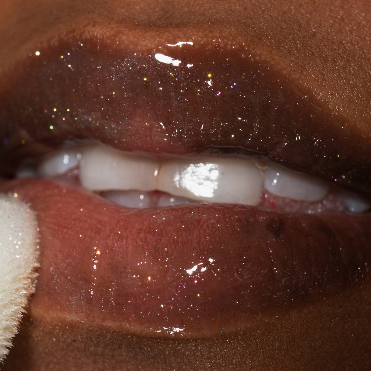 Nahaufnahme von Lippen einer Person mit dunklem Teint mit transparent glitzerndem Glazed Yum Lipgloss von LH Cosmetics.