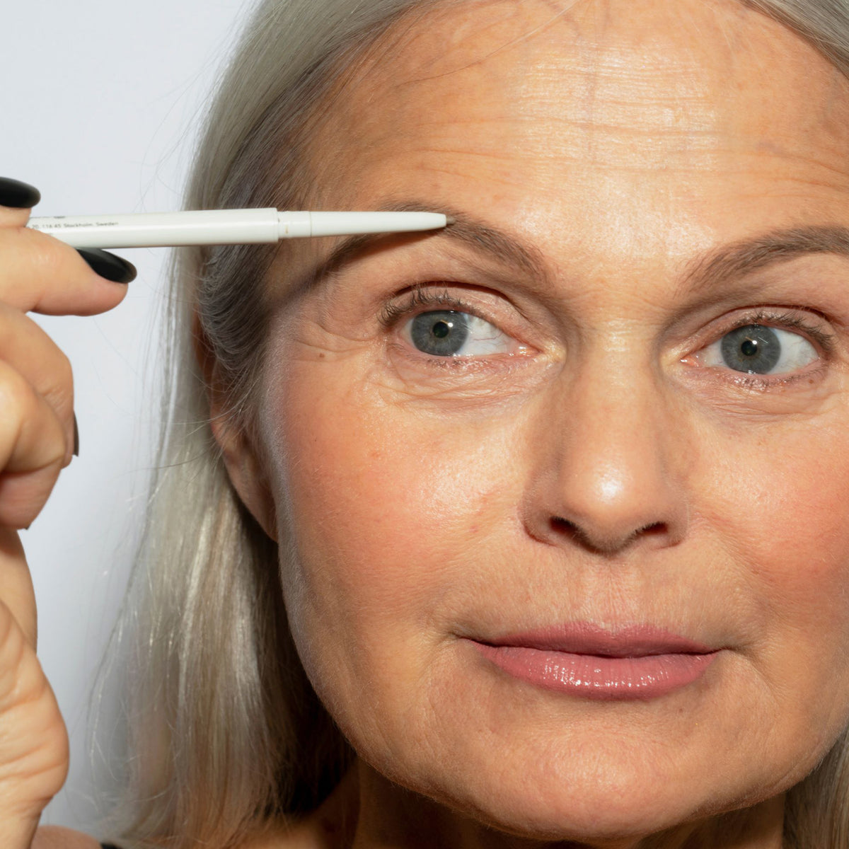 Eine Frau mit hellem Hautton und grauem Haar trägt den Infinity Brow Pen Greige auf ihre Augenbrauen.