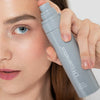 Eine Frau hält eine Sprühflasche „LH Cosmetics On Set – Subtle Glow Setting“ in die Nähe ihres Gesichts und betont so ihr frisches, natürliches Make-up.