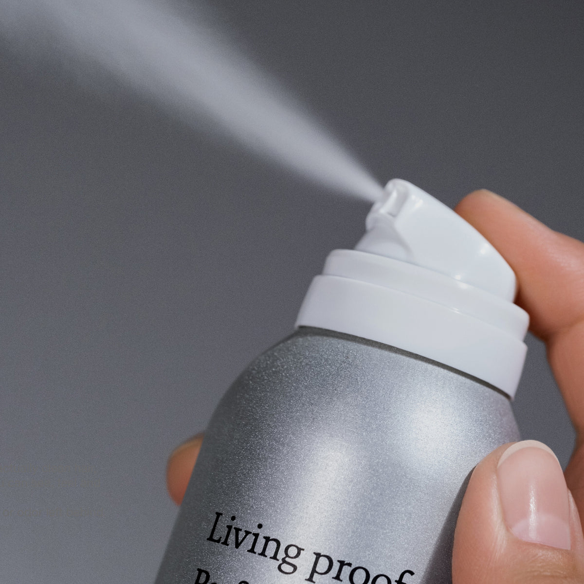 Eine Hand drückt mit silberner Sprühdose das Living Proof Perfect Hair Day Advanced Clean Dry Shampoo in die Luft.
