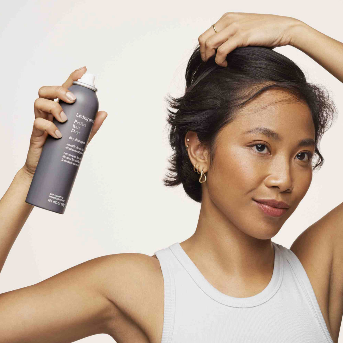 Eine Frau hebt ihr Haar mit einer Hand an und sprüht mit der anderen Living Proof Perfect Hair Day Dry Shampoo auf.