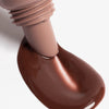 Nahaufnahme des Applikators des Lip Glow Oil Balm Honey streicht durch die braune Textur auf weißer Oberfläche