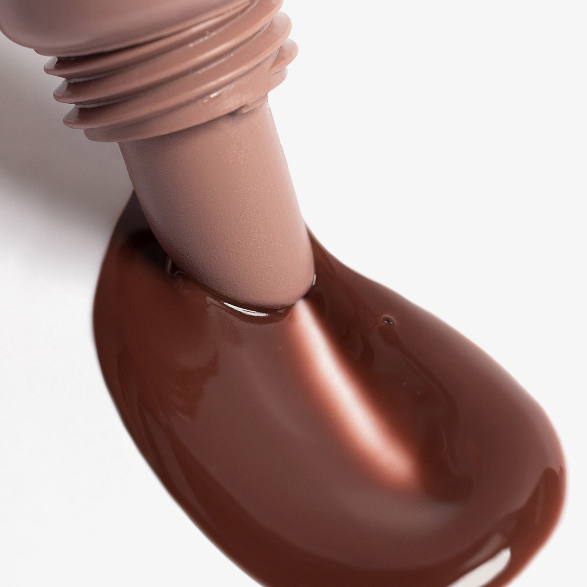 Nahaufnahme des Applikators des Lip Glow Oil Balm Honey streicht durch die braune Textur auf weißer Oberfläche
