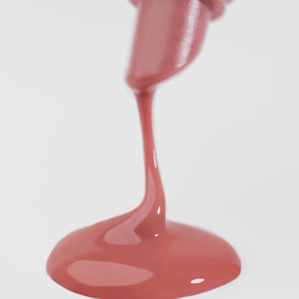 Eine Nahaufnahme des Lip Glow Oil Balm SPF30 1 Fudge von Lumene, der aus der Flasche fließt und eine kleine Pfütze auf einer weißen Fläche bildet.