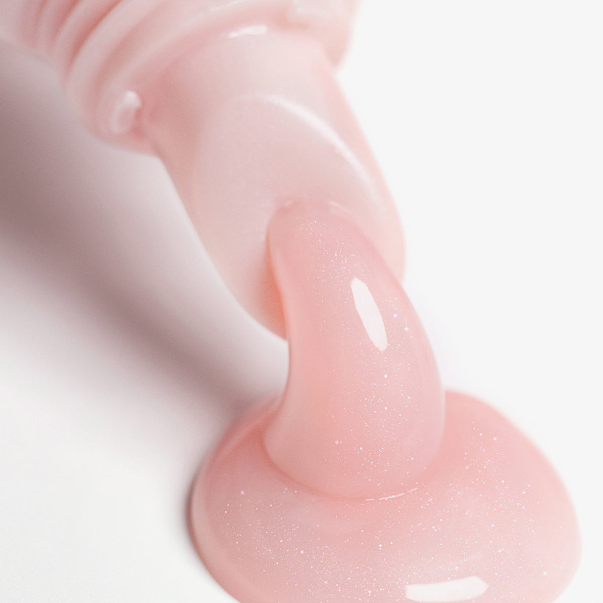 Die schimmernde hellrosa Textur des Lip Glow Oil Balm tritt aus dem Applikator auf eine weiße Oberfläche