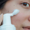 Eine Person trägt Lumene NORDIC HYDRA [LAHDE] Arctic Aqua Foaming Cleanser mit einem weißen Pumpspender auf die Wange auf.
