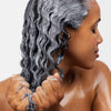 Eine Frau trägt maria nila Coils & Curls Co-Wash mit beiden Händen auf ihr nasses, lockiges Haar auf.