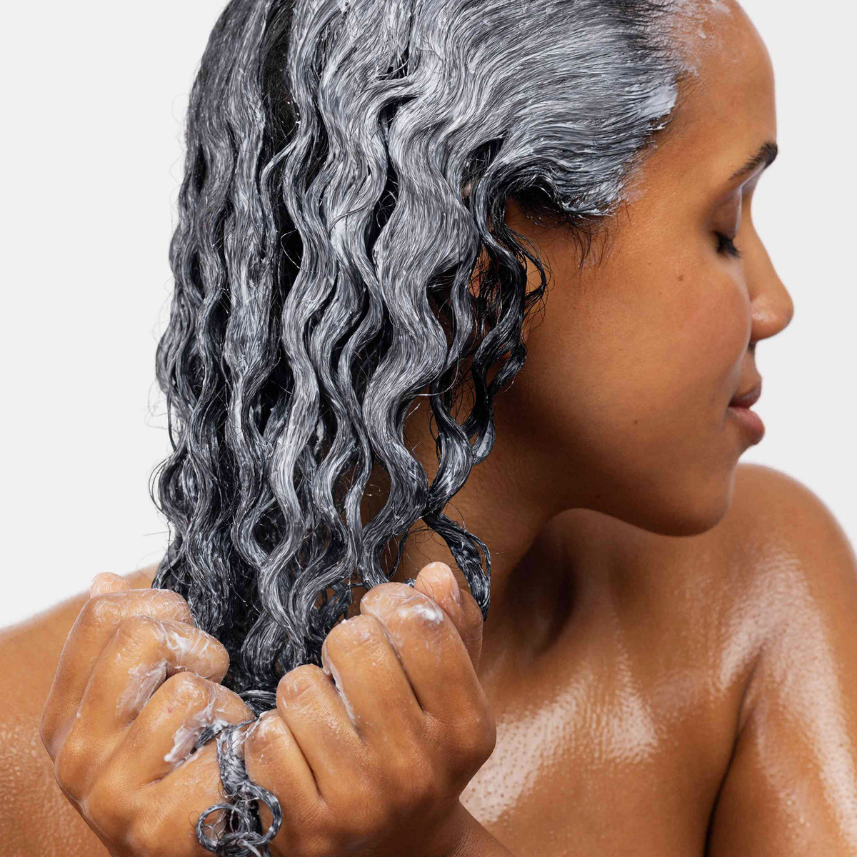 Eine Frau trägt maria nila Coils & Curls Co-Wash mit beiden Händen auf ihr nasses, lockiges Haar auf.