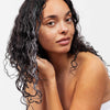 Eine Frau massiert die weiße maria nila Coils & Curls Oil-In-Cream in ihr lockiges, dunkles Haar ein.