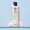 Eine rosafarbene Flasche von maria nila Luminous Colour Shampoo mit Schaum steht vor einem blauen Hintergrund.