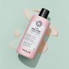 Eine rosafarbene Flasche maria nila Pure Volume Conditioner ist auf einem hellgrünen Hintergrund abgebildet, unter dem Conditioner verschmiert ist.