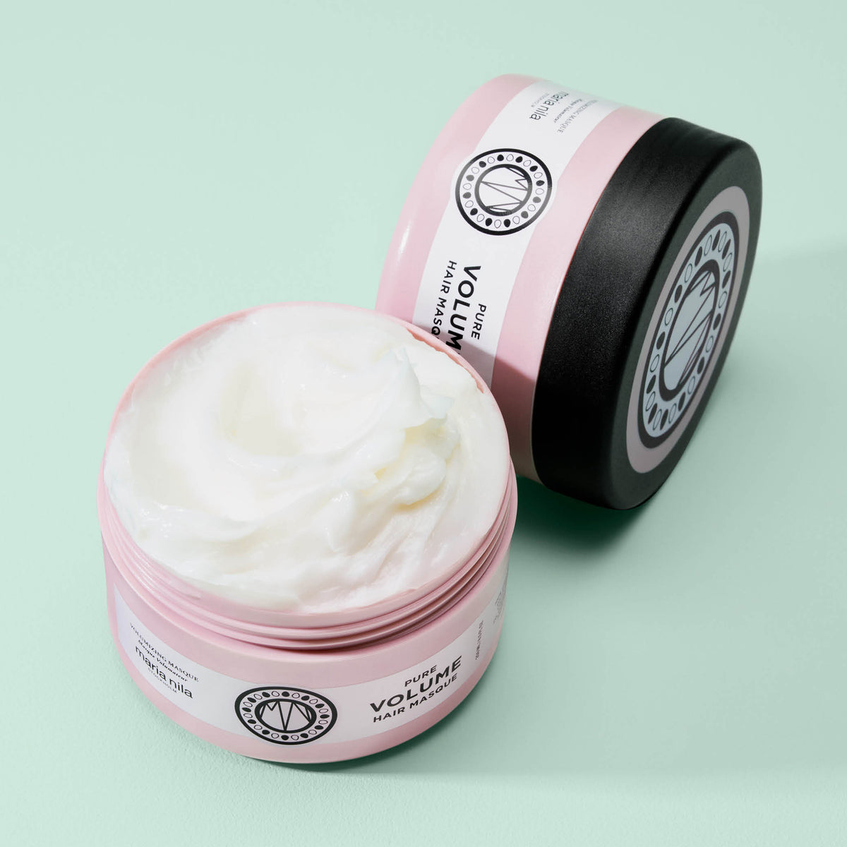Geöffneter Tiegel der maria nila Pure Volume Masque zeigt weiße Creme, weitere Tiegel auf einer hellgrünen Fläche.