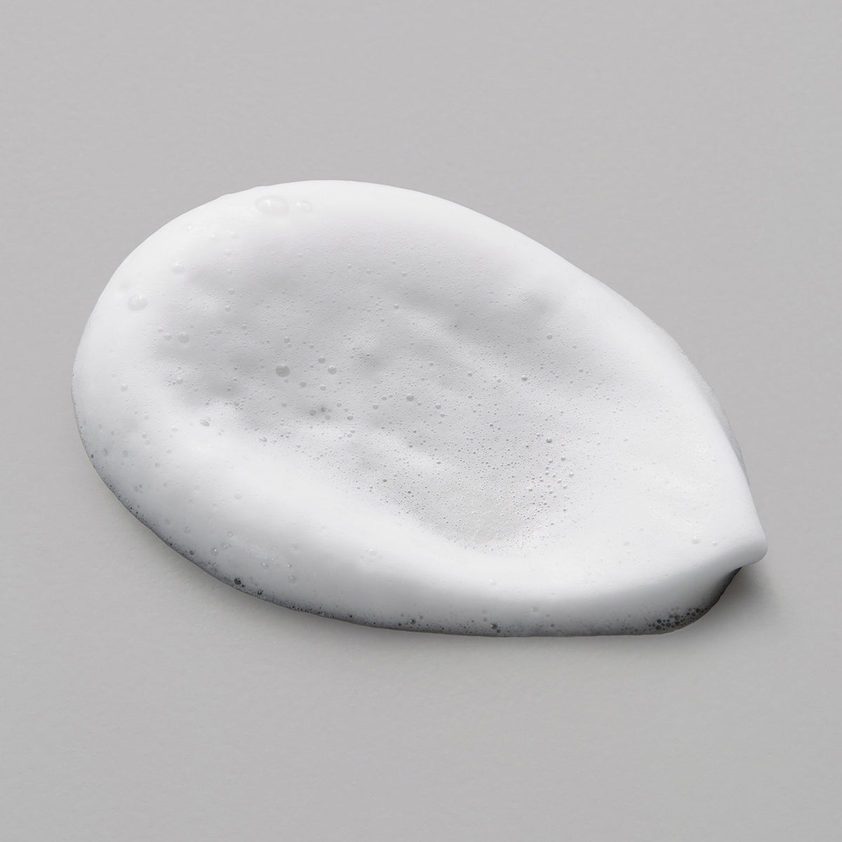 Weißer Schaumklecks des Maria Nila Pure Volume Mousse auf einer glatten, hellgrauen Oberfläche.