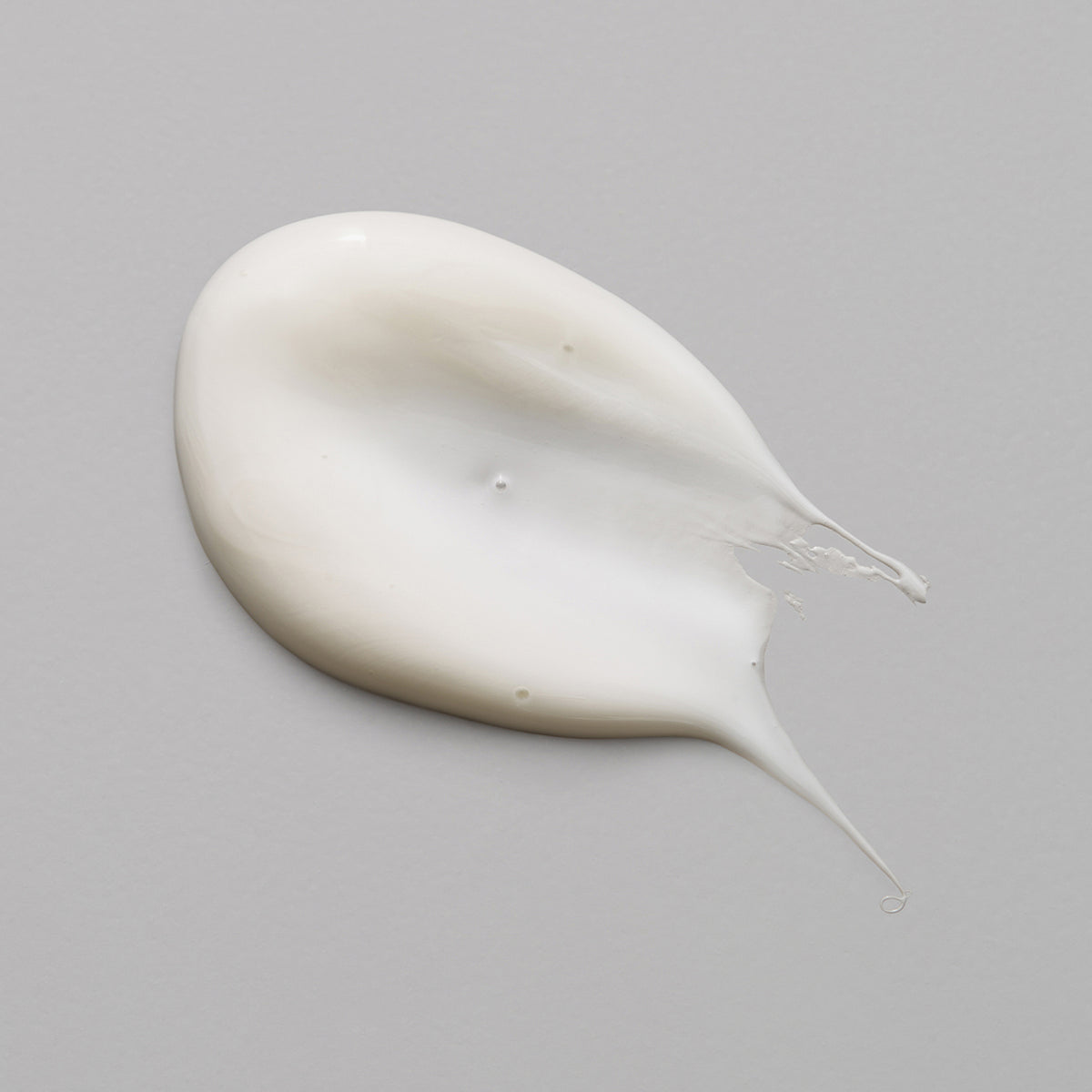 Cremeweißer Klecks  der maria nila Schist Fibre Cream auf einer glatten, hellgrauen Oberfläche.