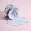 Ein geöffneter Tiegel der lavendelfarbenen maria nila Sheer Silver Masque ergießt sich über eine pastellrosa Oberfläche.