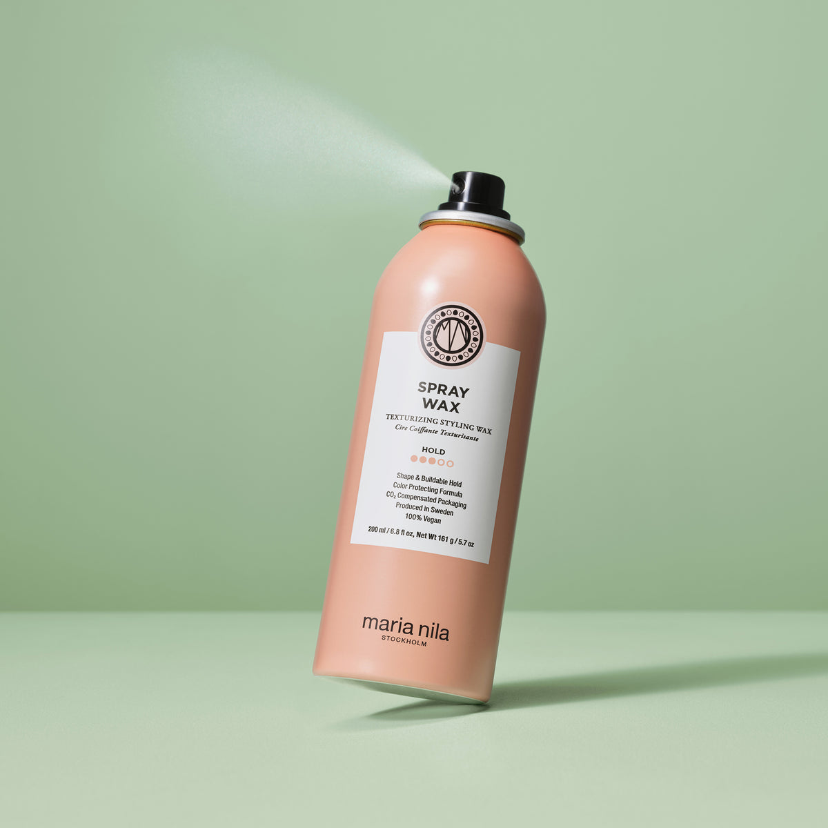 Eine Dose maria nila Spray Wax versprüht einen Nebel vor einem grünen Hintergrund.