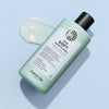Eine Flasche maria nila True Soft Conditioner liegt auf einer hellblauen Fläche neben einem Klecks der Spülung.