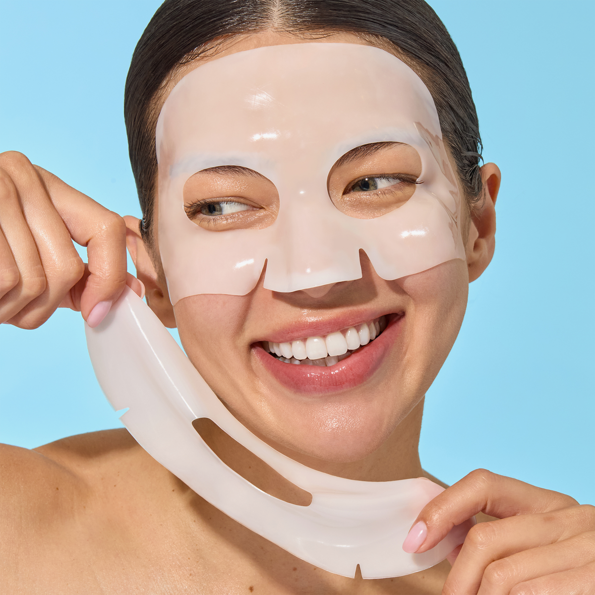 Eine lächelnde Frau entfernt die Mario Badescu Advanced Collagen Hydrogel Mask 3 Pack vor einem hellblauen Hintergrund.