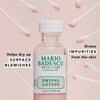 Ein Fläschchen Drying Lotion von Mario Badescu ist umgeben von rosa Wattestäbchen auf einem hellrosa Hintergrund.
