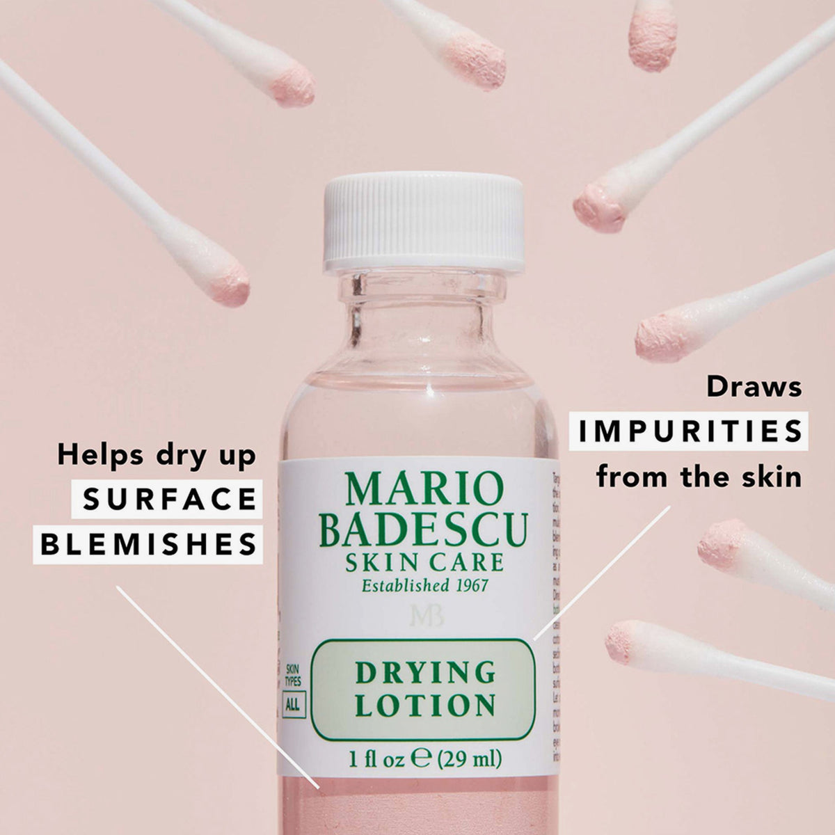 Ein Fläschchen Drying Lotion von Mario Badescu ist umgeben von rosa Wattestäbchen auf einem hellrosa Hintergrund.