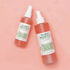 Zwei Flaschen Mario Badescu Gesichtsspray mit Aloe, Kräutern und Rosenwasser sind vor einem rosa Hintergrund abgebildet.